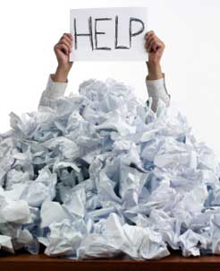 person, surrounded by crumpled writing paper, holding up help sign
